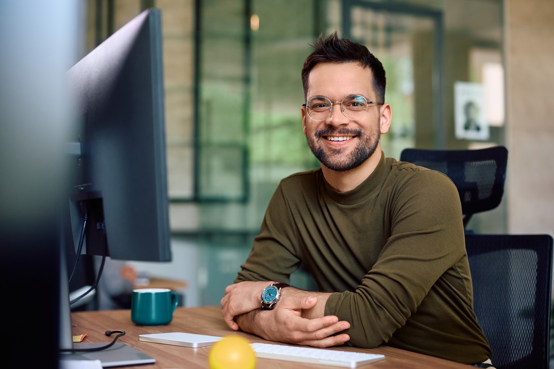 Happy male entrepreneur at  his office desk looking at camera.